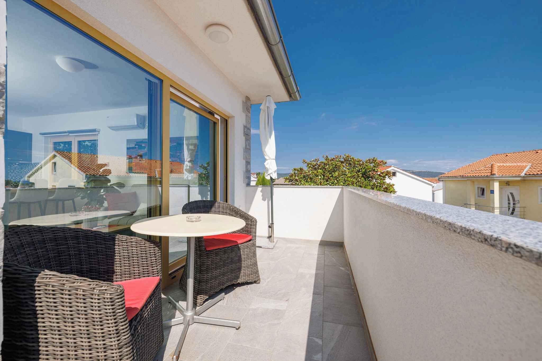 A balcony with wicker furniture and a glass table, overlooking a residential area.
