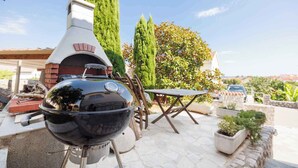 Una parrilla y un horno de ladrillo en un espacio exterior con plantas en macetas y una mesa.