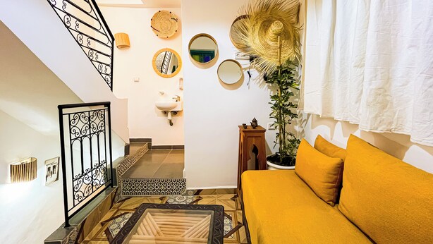 A living room with a staircase, a sofa, a plant, and a mirror on the wall. - Porte Principale  (Marrakech)