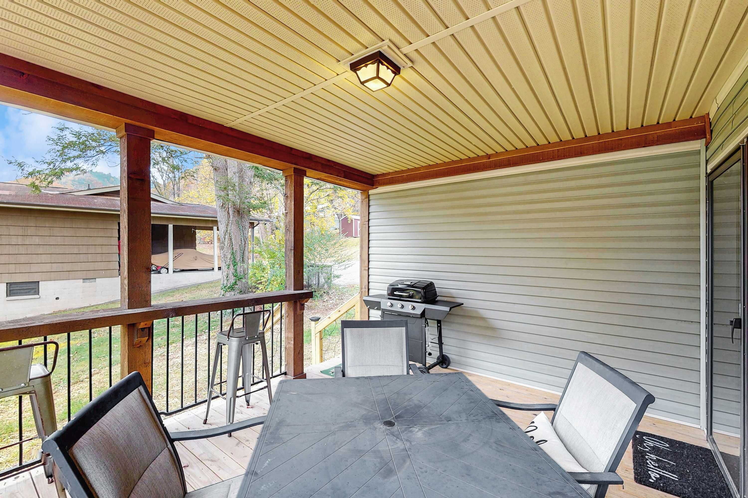 A covered patio with a table and chairs, a grill, and a view of the neighborhood.
