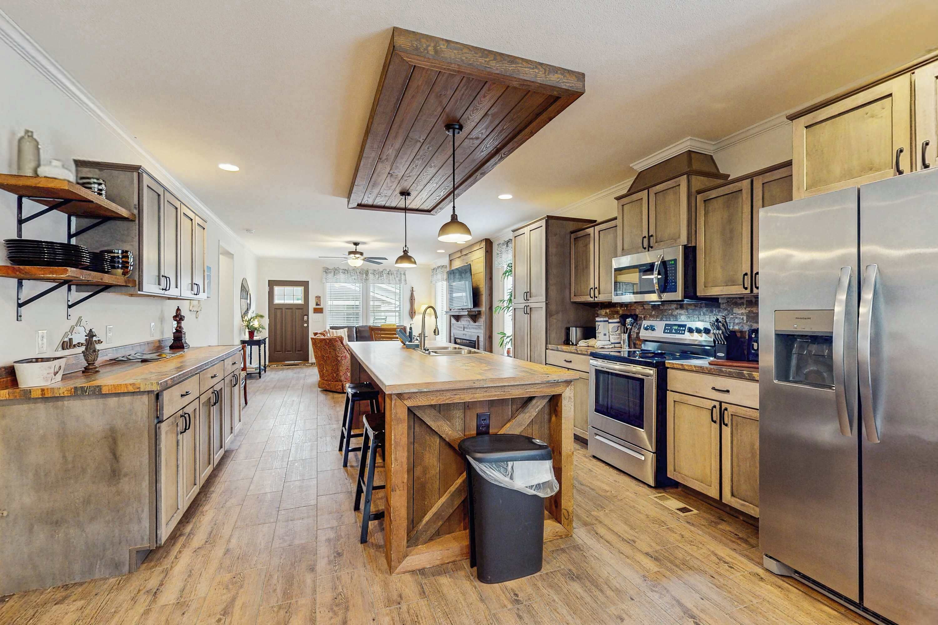 Une cuisine spacieuse avec des meubles en bois, un grand îlot central, des appareils électroménagers en acier inoxydable et un plafond au style rustique.