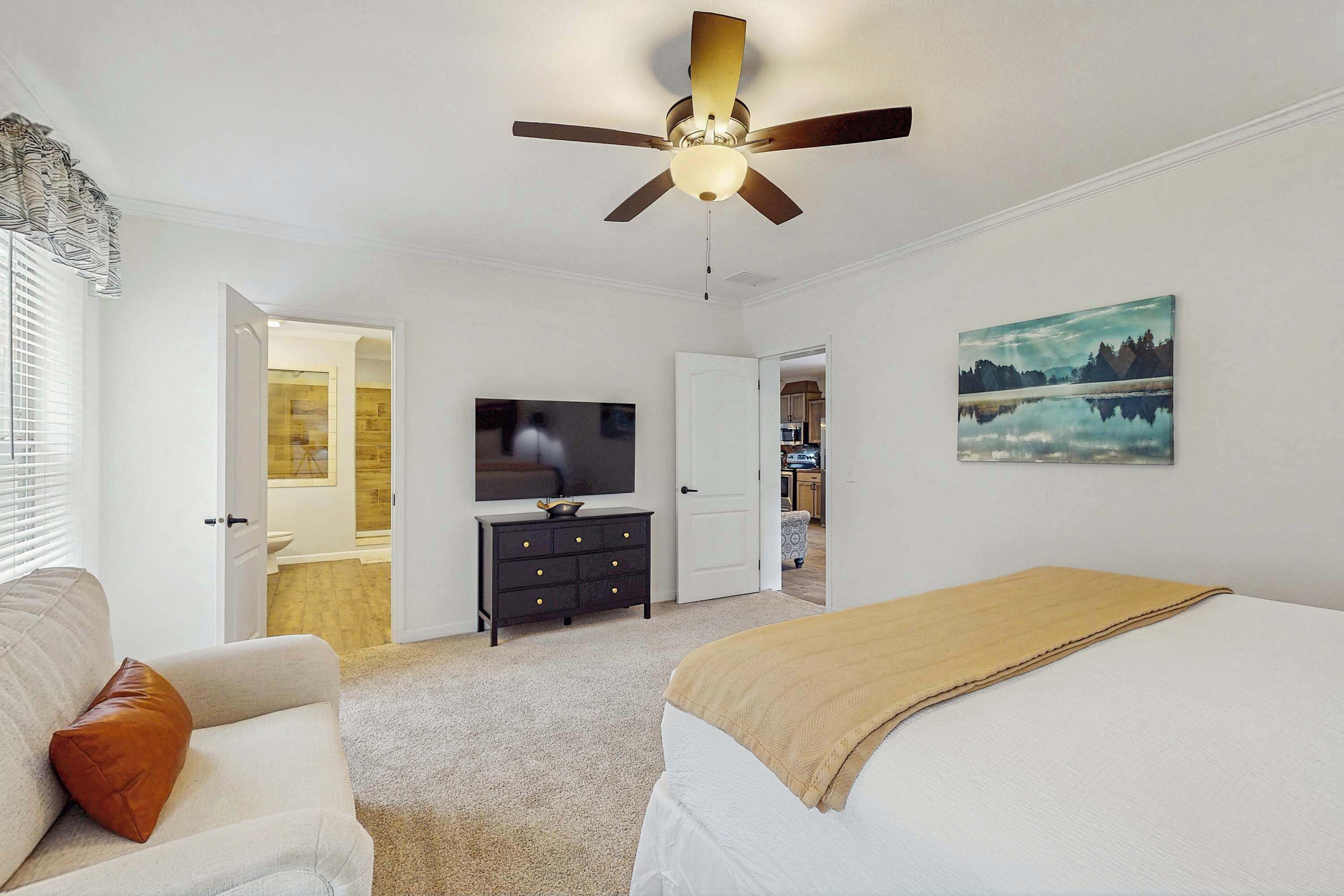 A bedroom with a bed, a sofa, a ceiling fan, a TV, and a painting.