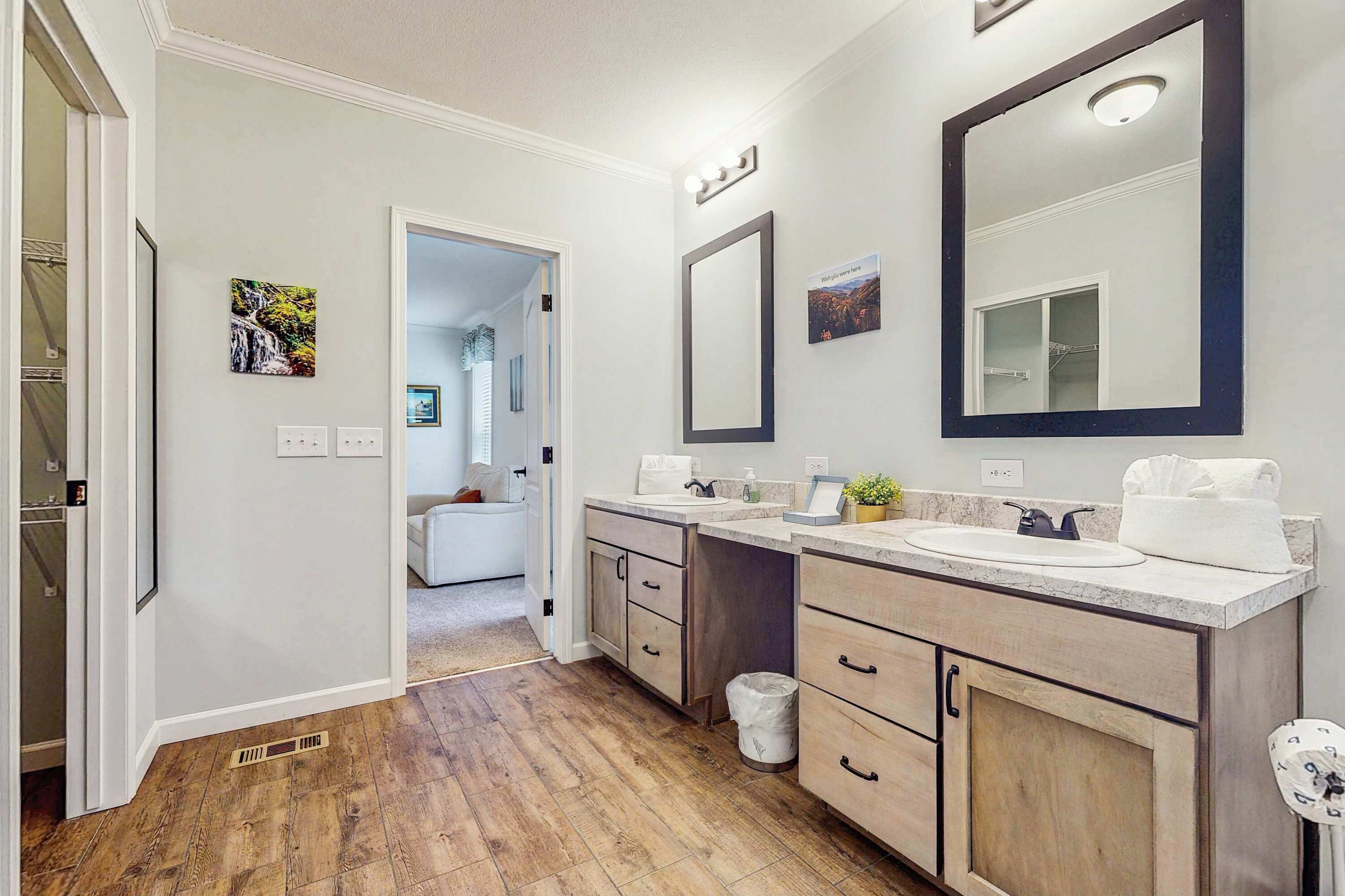 A modern bathroom with two sinks, a large mirror, and a walk-in closet.