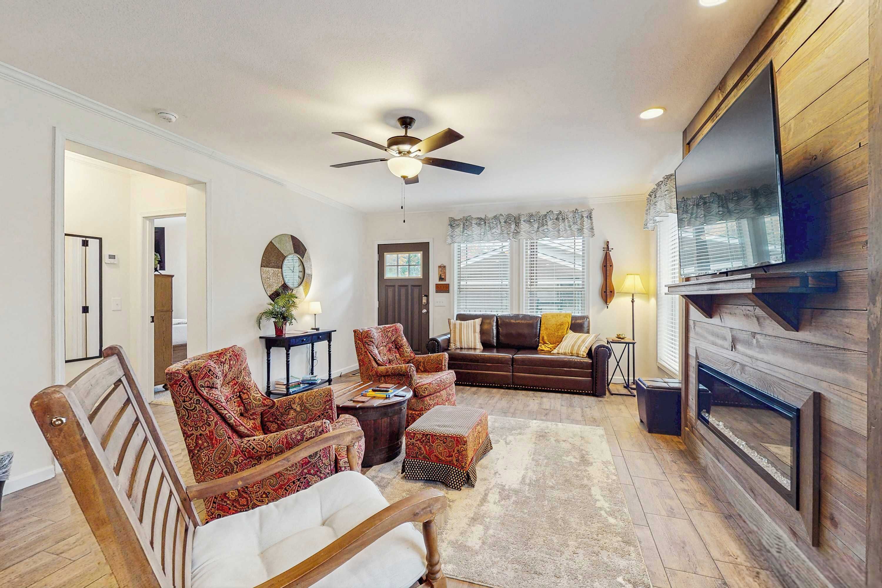 A living room with a ceiling fan, a fireplace, a TV mounted on the wall, and a large mirror.