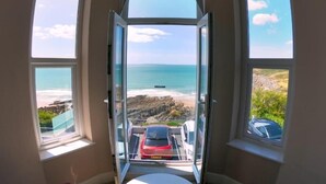 Ein Zimmer mit einem großen Erkerfenster, das Blick auf Strand und Meer bietet.