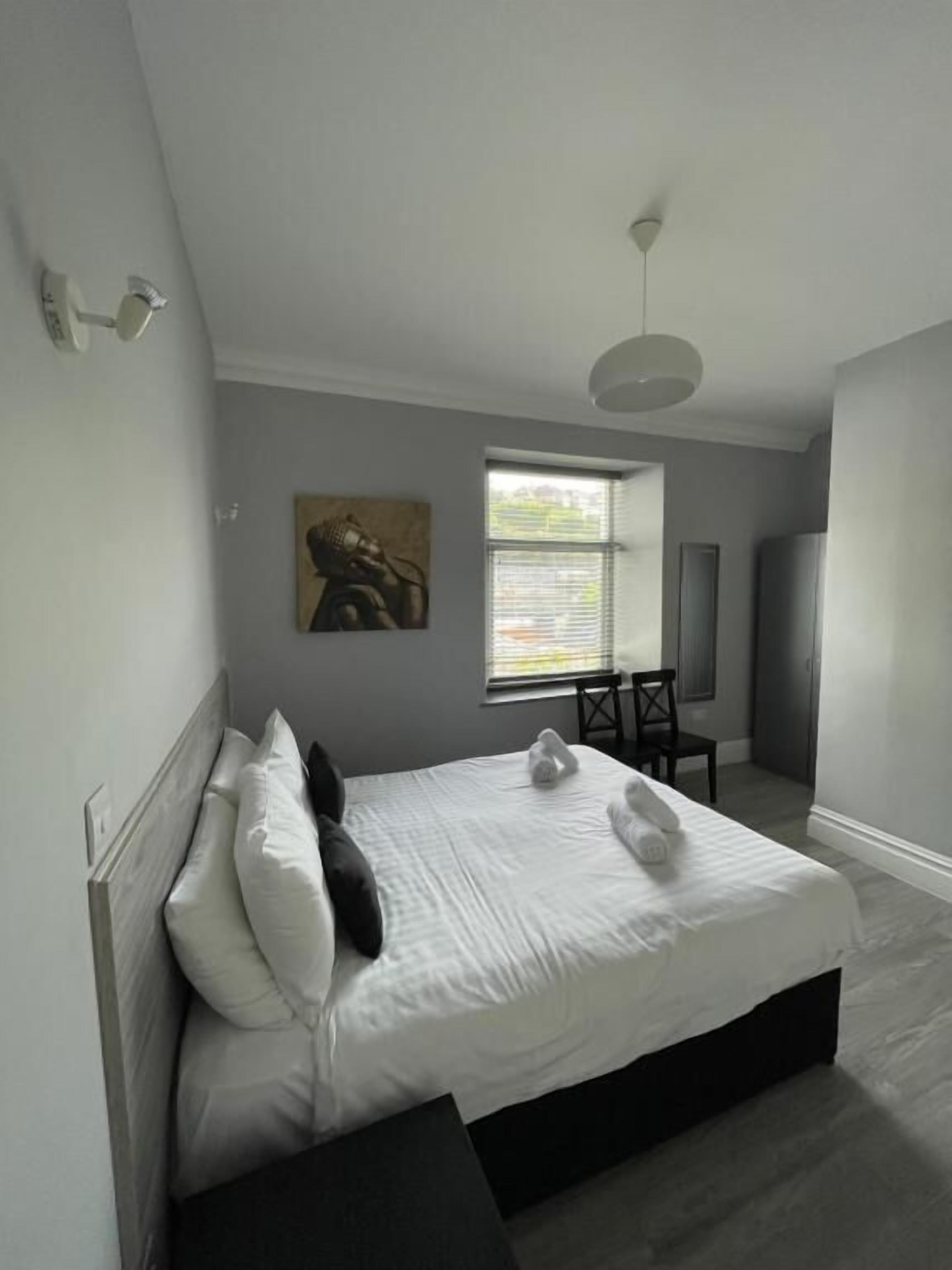 Une chambre à coucher moderne avec un grand lit, une fenêtre, une chaise et un tableau accroché au mur.