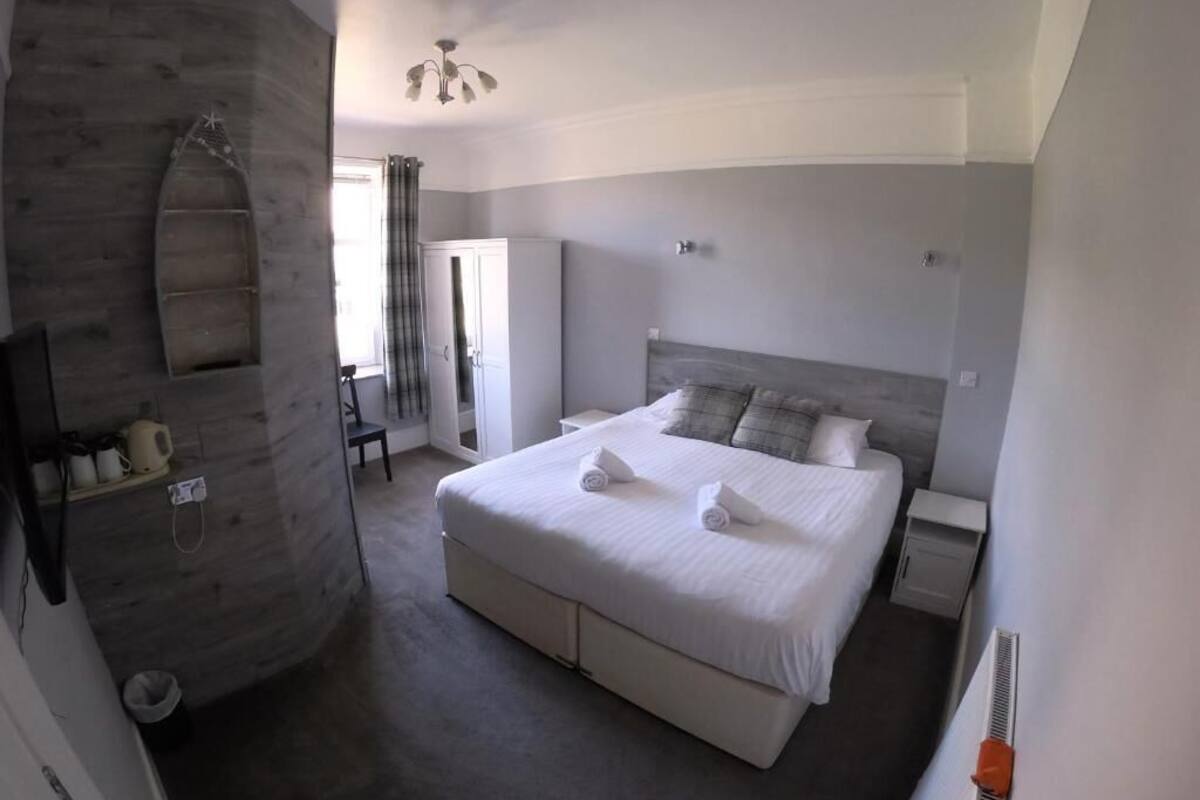 A bedroom with a large bed, a built-in bench, a wardrobe, and a shower area.