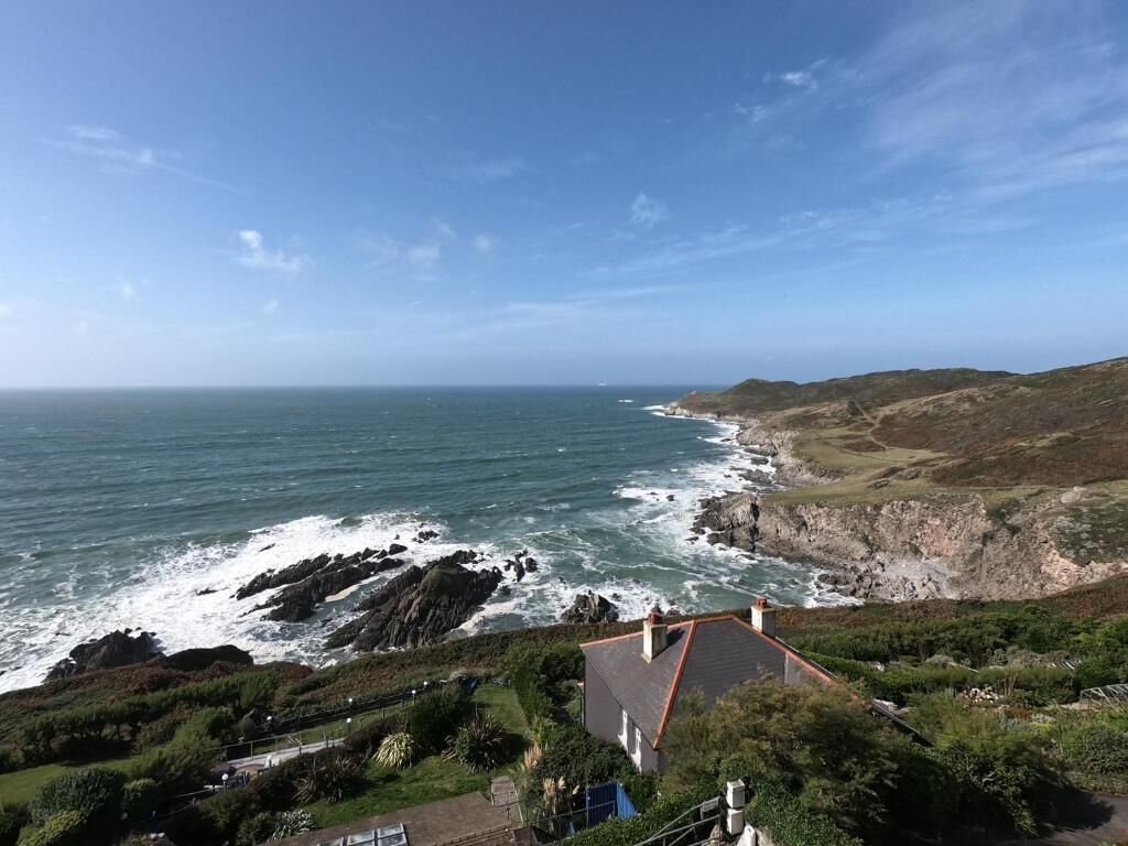 Une vue côtière avec une maison surplombant la mer, des falaises rocheuses et un ciel dégagé.