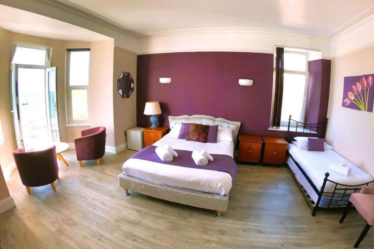 A bedroom with a large bed, a bedside table with a lamp, a chair, and a window.