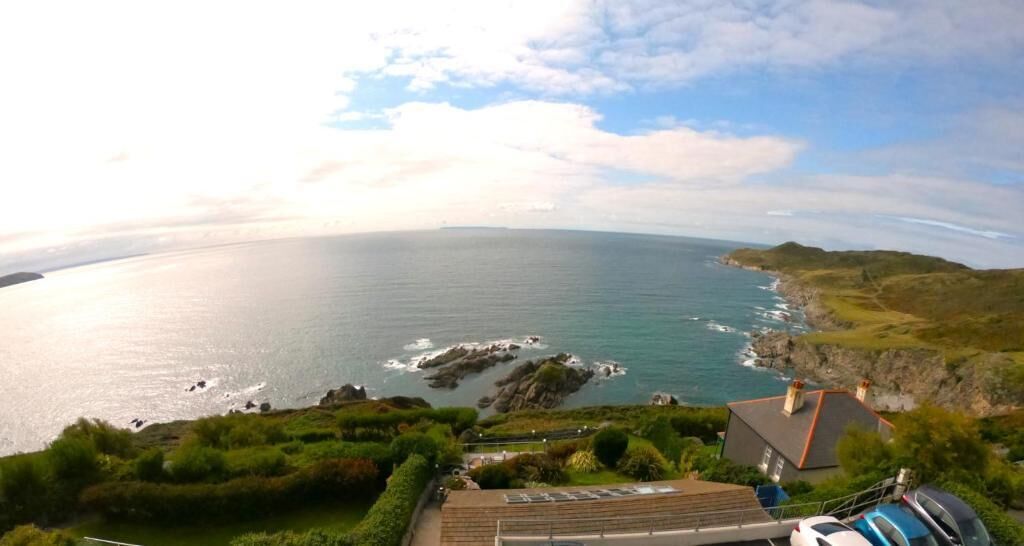 A coastal landscape with a view of the sea, rocky coastline, and a building with a sloped roof.