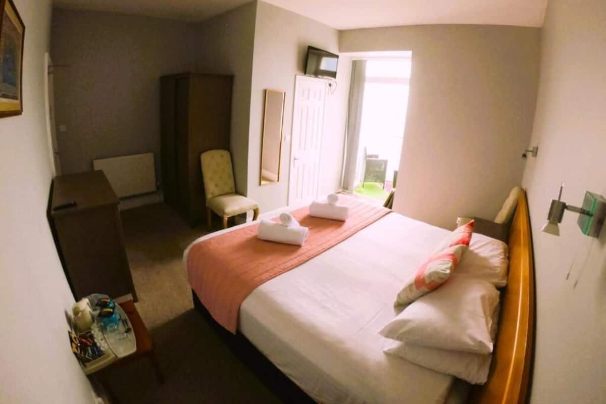 A hotel room with a bed, a chair, a desk, a wardrobe, and a window.