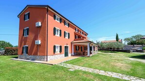 Un edificio a più piani con facciata rossa, un patio coperto e un viale in pietra che conduce all'ingresso.