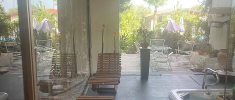Uma área de spa com bancos de madeira, uma banheira de hidromassagem e uma parede de vidro com vista para o jardim externo.
