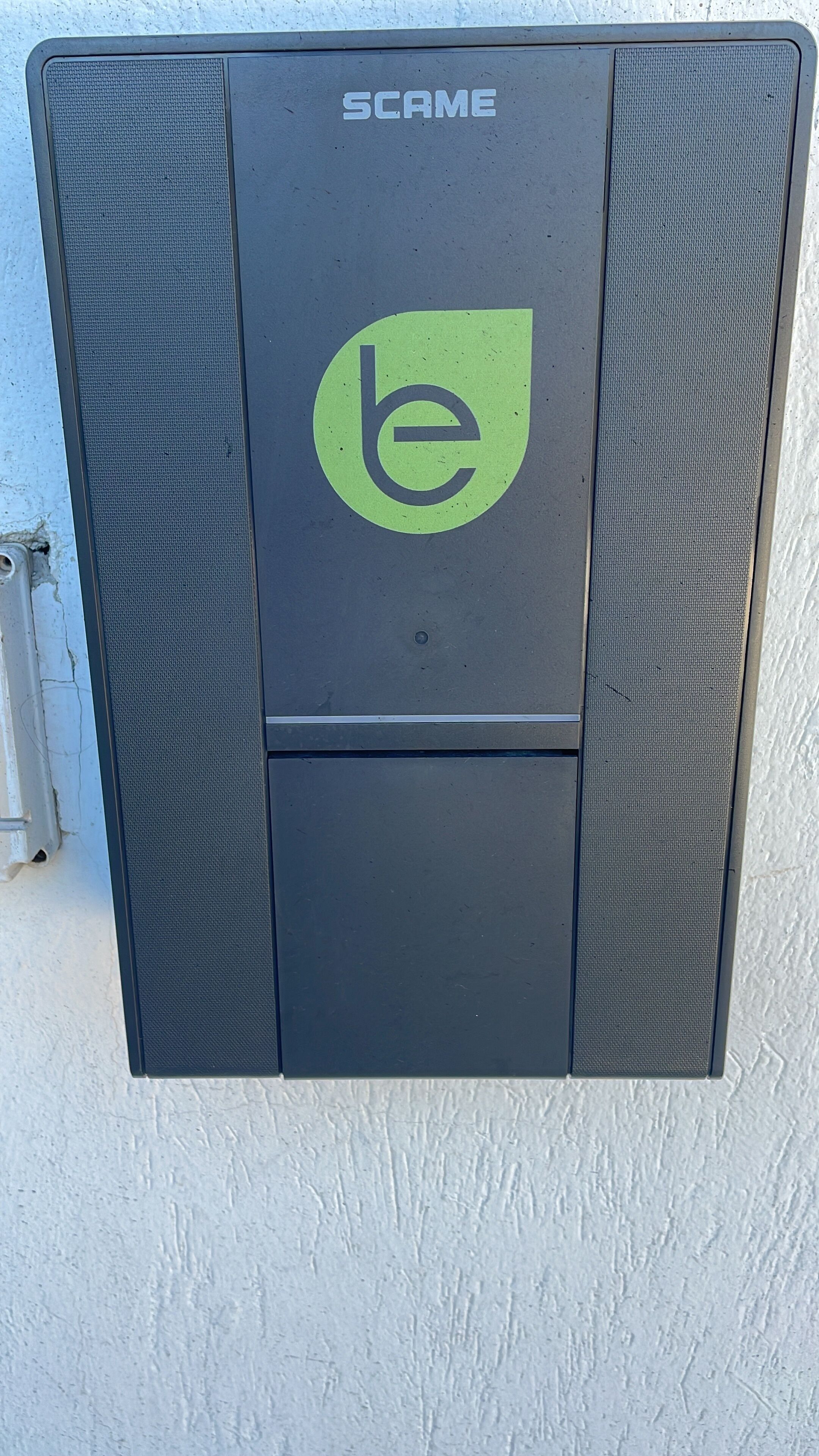 Una unidad exterior negra con el nombre de marca "SCAME" y un logotipo con las letras 'b' y 'e' en minúscula.