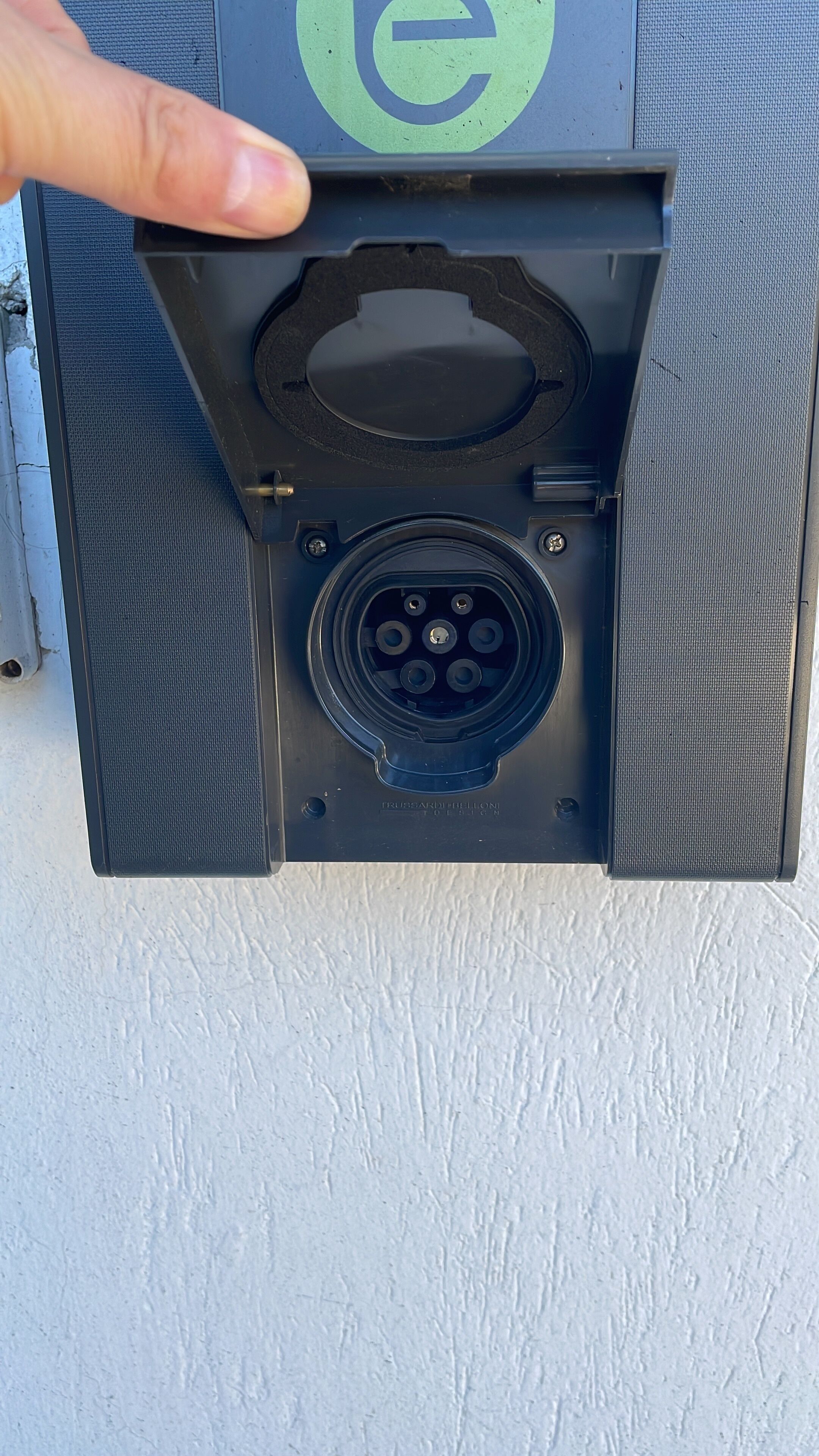 Caja eléctrica exterior negra con un enchufe circular y una mano sosteniéndola.