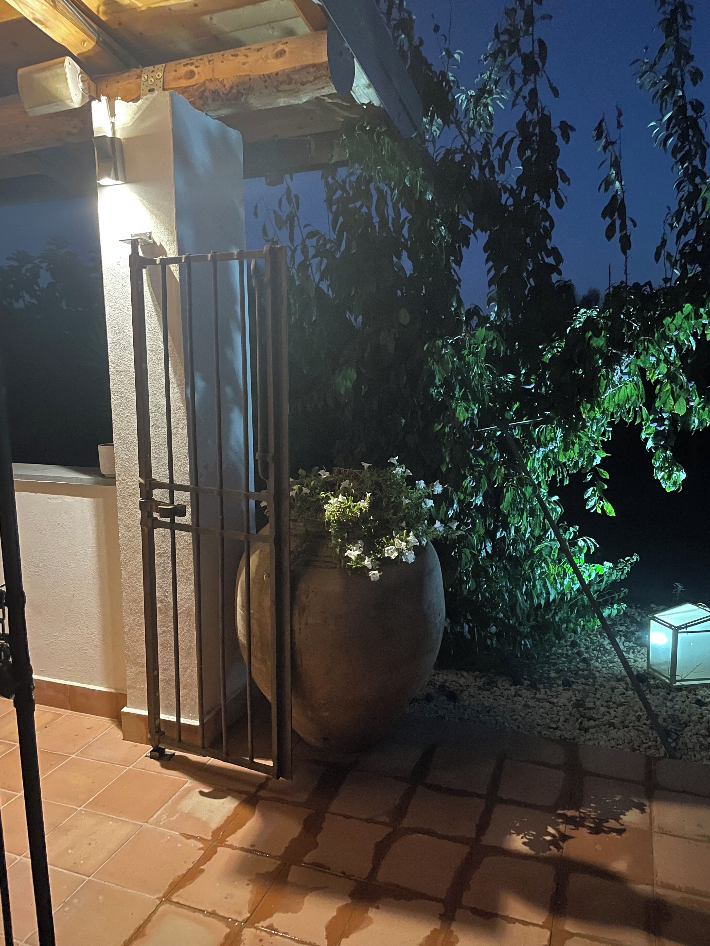 Une entrée fermée par un portail, agrémentée d’un grand bac à fleurs et d’une petite structure illuminée.