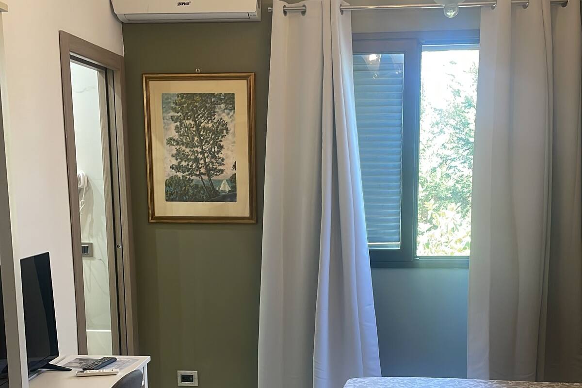 Une chambre à coucher comprenant un lit, un bureau, une chaise, un lustre, une fenêtre avec des rideaux et un tableau encadré accroché au mur.