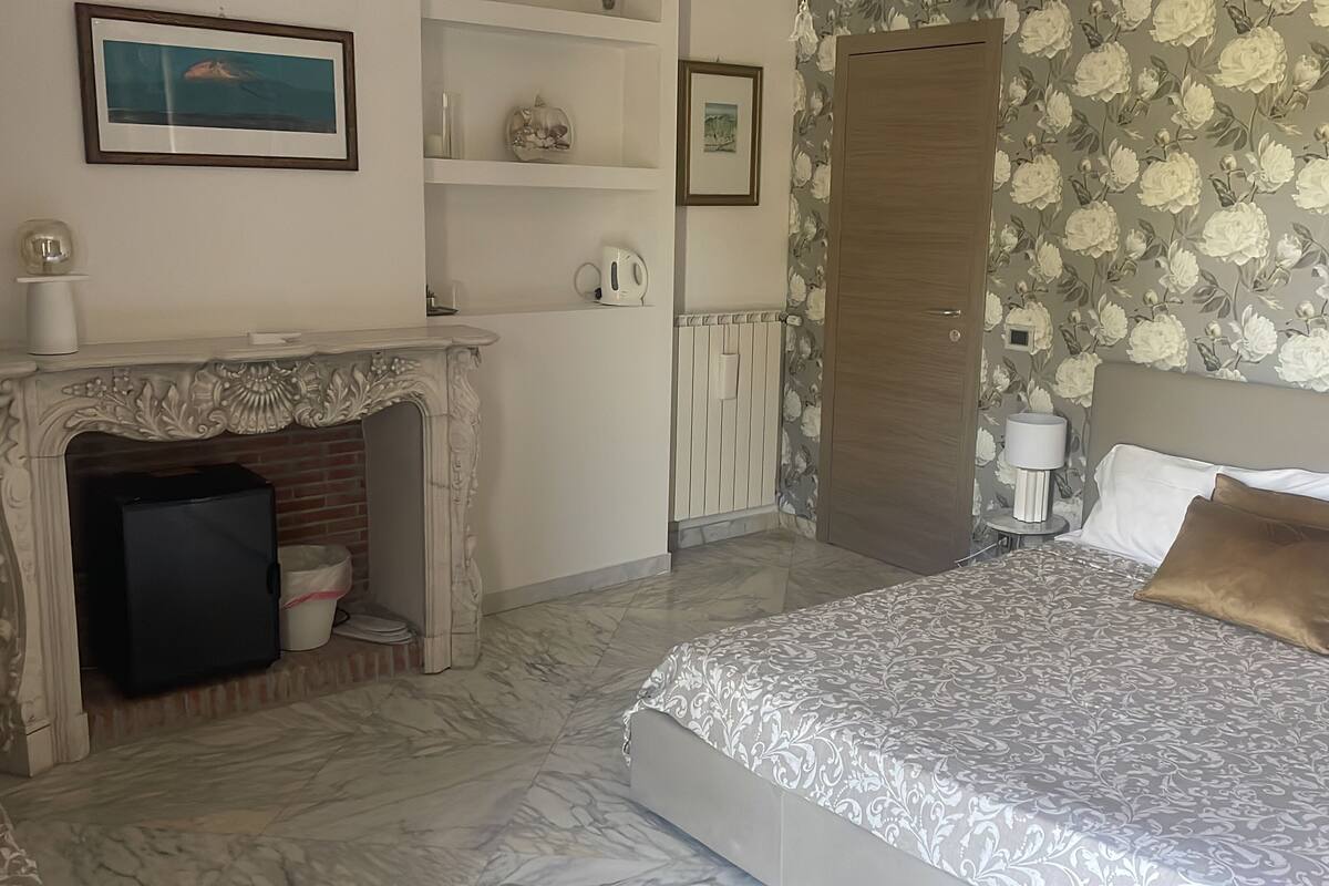Une chambre à coucher avec un lit, une cheminée, une armoire et un papier peint à motifs floraux.