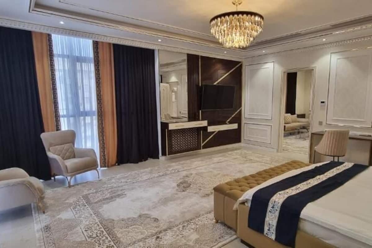 A spacious bedroom with a large bed, a seating area with chairs, a television, and a wardrobe.