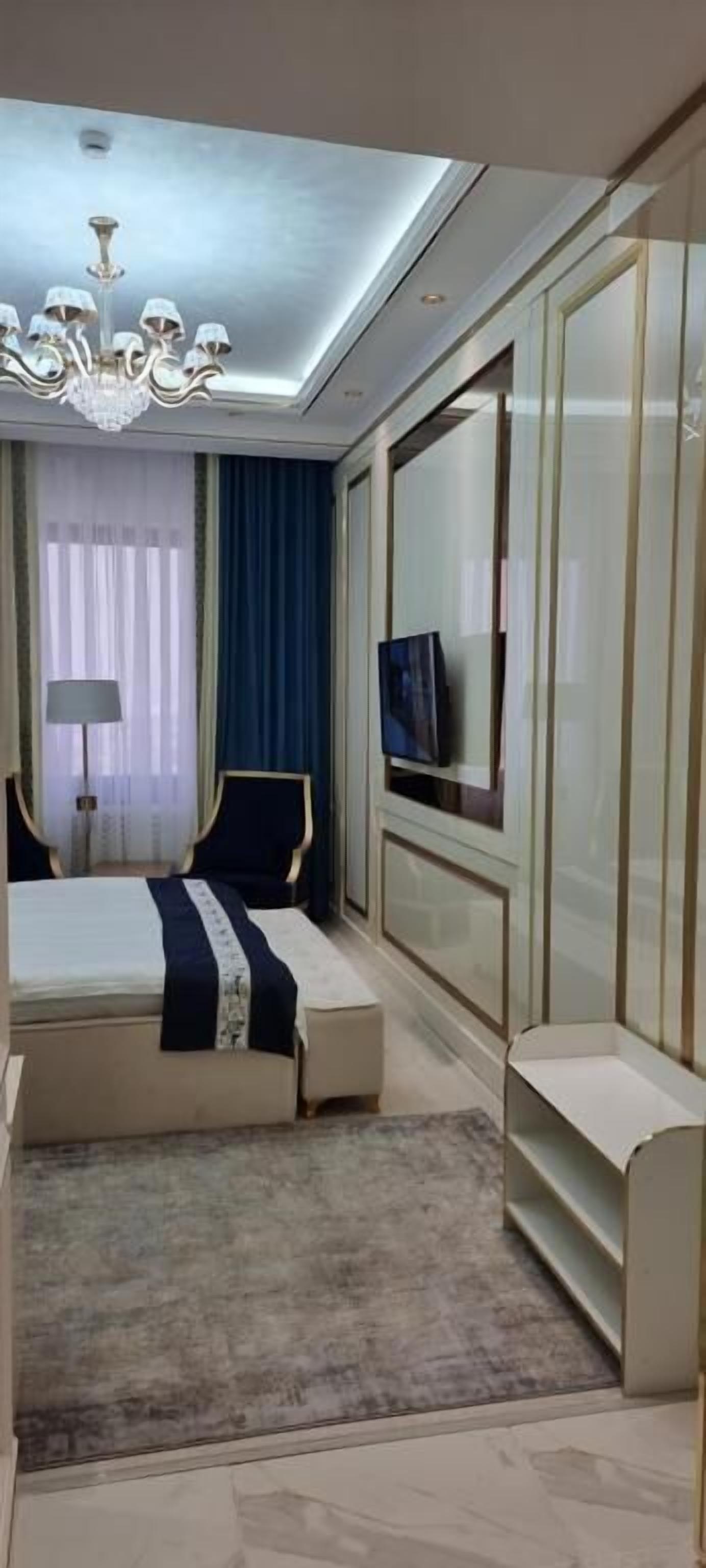 A modern bedroom with a bed, a TV, a chandelier, and a large mirror.