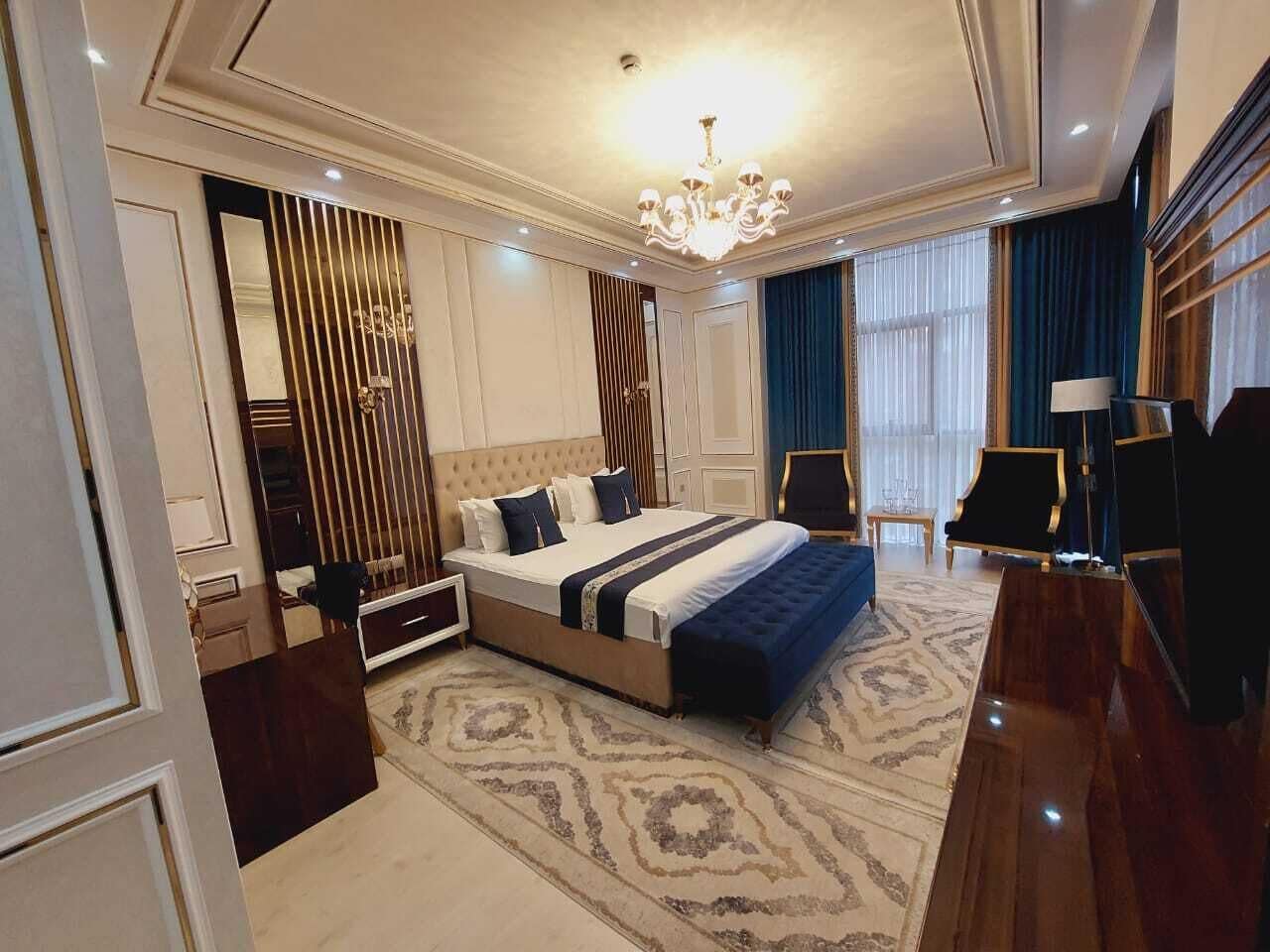 A spacious bedroom with a large bed, a chandelier, a desk, and a chair.
