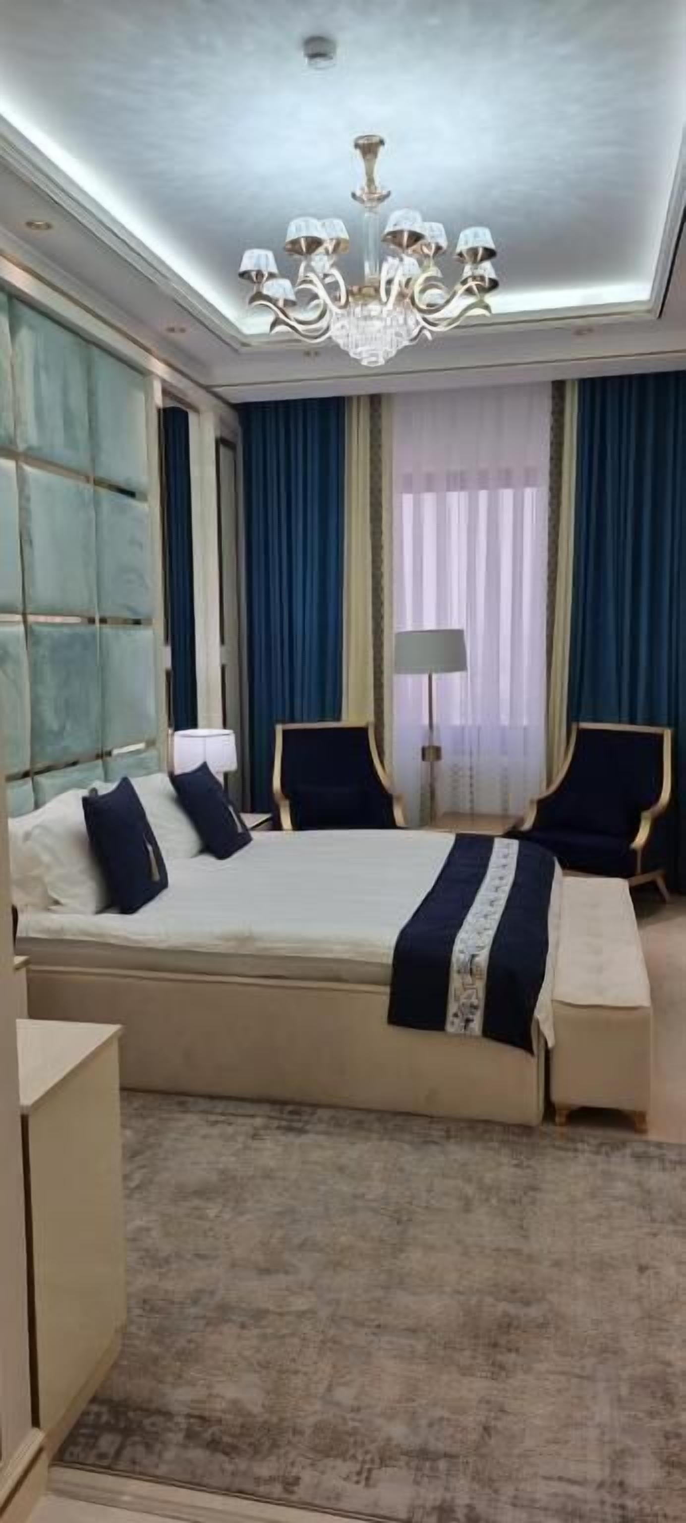 Een ruime slaapkamer met een groot bed, twee fauteuils, een nachtkastje en een kroonluchter.