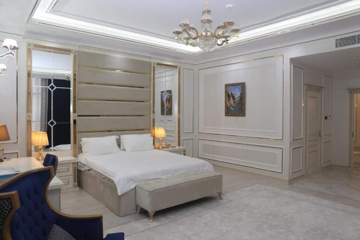 A spacious bedroom with a large bed, bedside tables, a desk, and a chair.