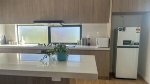Een moderne keuken met houten kastjes, een wit aanrecht, een ingebouwde magnetron en een koelkast.