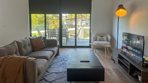 Een moderne woonkamer met een bank, een salontafel, een tv-meubel en een grote glazen schuifdeur die leidt naar een terras.
