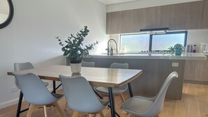 Een moderne keuken met een houten tafel en stoelen, een plant in een pot en een raam met uitzicht op de stad.