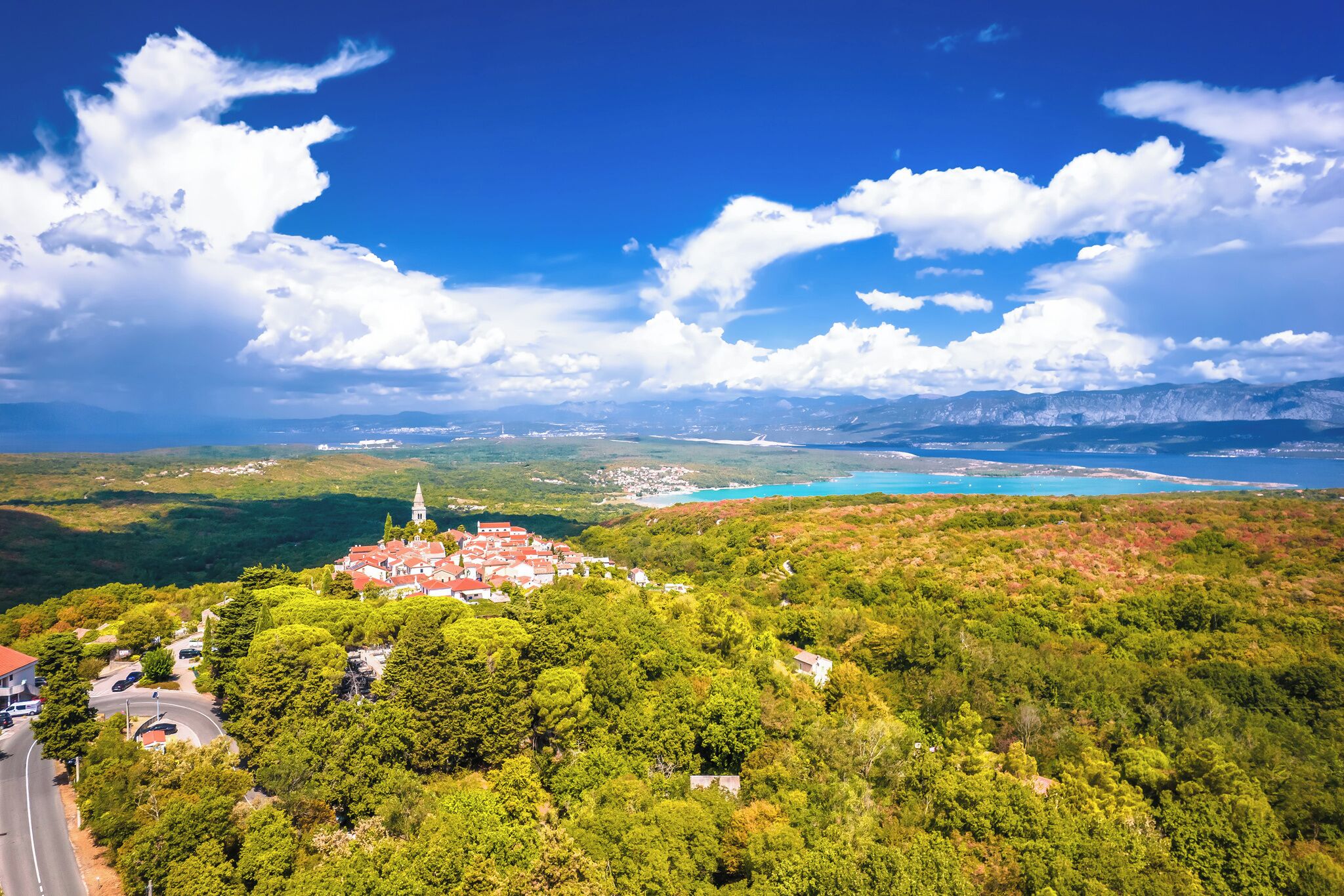 A town with a prominent church, surrounded by lush greenery and a clear blue sky.
