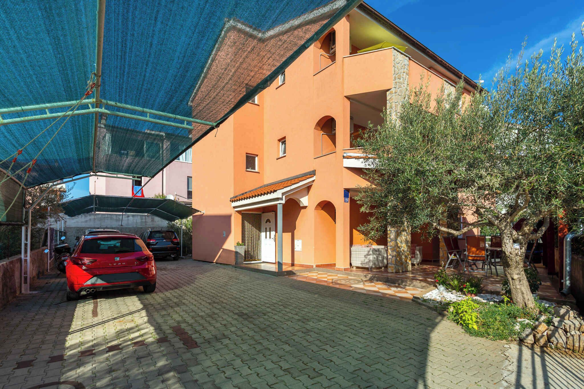 A building with a covered parking area, a red car parked in front, and a tree to the right.