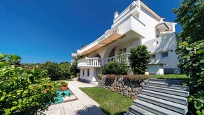 Une maison moderne à deux étages, dotée d’une piscine, d’un mur en pierre et d’un escalier en pierre menant à l’entrée.