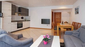 A modern living room with grey sofas, a coffee table with a pink flower vase, and a dining area with a wooden table and chairs. - Holiday Flat Guesthouse Apartment Halilagic (Krk)