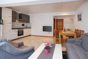 A modern living room with grey sofas, a coffee table with a pink flower vase, and a dining area with a wooden table and chairs. - Holiday Flat Guesthouse Apartment Halilagic (Krk)