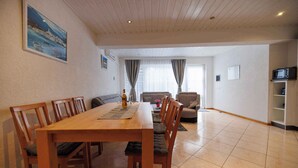A dining area with a wooden table and chairs, a sofa, and a kitchen area with a microwave. - Holiday Flat Guesthouse Apartment Halilagic (Krk)