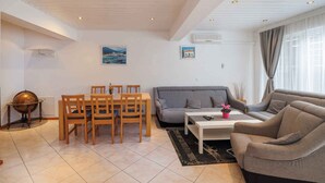 A living room with a grey sofa, a dining table with chairs, a coffee table, and a globe on a side table. - Holiday Flat Guesthouse Apartment Halilagic (Krk)