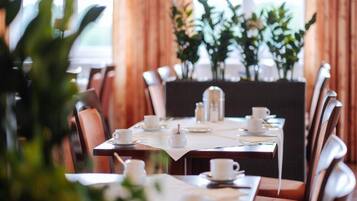 A dining area with tables set for service, chairs, and a large window with curtains.