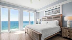 A bedroom with a large bed, a view of the ocean, and a painting of birds on the wall. - Luxury 4BR Condo w/ private beach access & heated pool (Gulf Shores)
