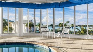 A poolside area with a view of a body of water, palm trees, and a clear sky. - Luxury 4BR Condo w/ private beach access & heated pool (Gulf Shores)