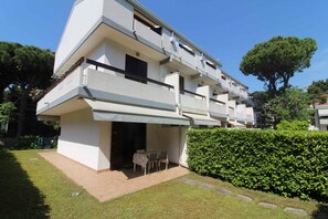 Un edificio residencial de varios pisos con balcones, una zona de estar al aire libre techada y un jardín bien cuidado.