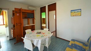 Un comedor con una mesa redonda, sillas blancas, una estantería de madera y un cuadro en la pared.
