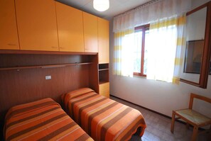 Una habitación con dos camas individuales, un armario de madera, una mesita y una silla.