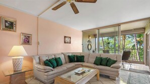 Un salón con un sofá seccional color beige, una mesa de centro de vidrio y un ventilador de techo.