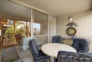 A balcony with a glass door, a round table, and four chairs. - Menehune Shores #301 - Oceanfront Shoreline Location with Inviting Living Spaces (Kihei, Maui)