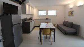 A compact living space with a kitchenette, dining area, and sofa. - Holiday apartment with air conditioning, terrace and garden (Lignano Sabbiadoro)
