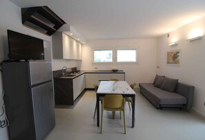 A compact living space with a kitchenette, dining area, and sofa. - Holiday apartment with air conditioning, terrace and garden (Lignano Sabbiadoro)