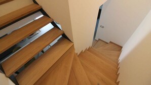 A wooden staircase with a modern design, leading to a room with white walls and a door at the bottom. - Holiday apartment with air conditioning, terrace and garden (Lignano Sabbiadoro)