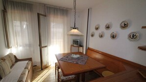 A cozy room with a wooden dining table, a sofa, a TV on a stand, and decorative plates on the wall. - Holiday apartment with air conditioning and balcony (Lignano Sabbiadoro)