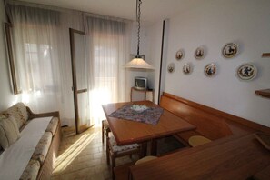 Ein gemütliches Zimmer mit einem Holztisch, einer Couch, einem Fernseher auf einem Schrank und dekorativen Tellern an der Wand.